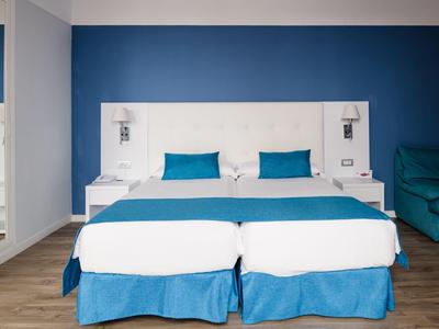 Modernes Schlafzimmer mit zwei Betten, weißen Kopfteil, blauen Kissen und Wand in kräftigem Blau.