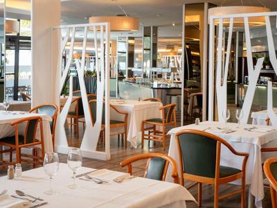 Elegantes Restaurant mit weißen Tischtüchern, Holzstühlen und moderner, heller Raumgestaltung.