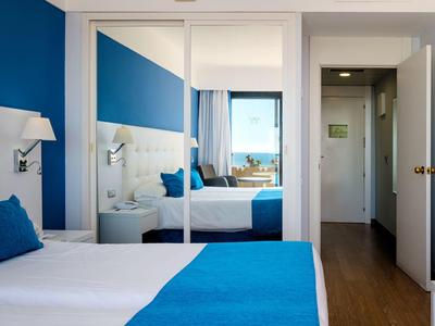 Helles Schlafzimmer mit großem Spiegel, weißer Wand, blauen Bettdecken und Holzboden.