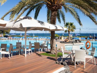 Modern outdoor area with tables, chairs, umbrellas, overlooking the pool and sea.