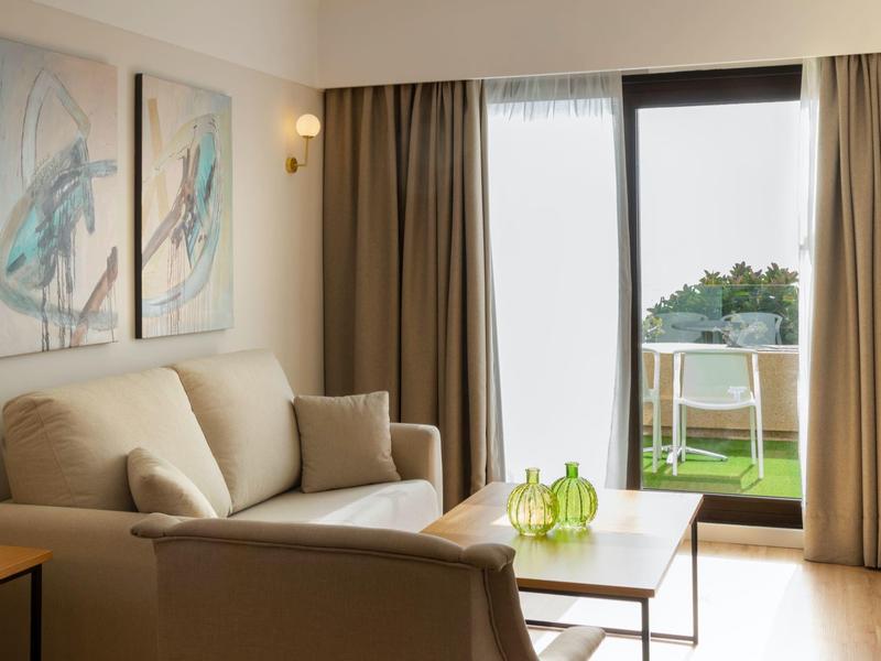 Helles Wohnzimmer mit beige Sofa, zwei Bildern an der Wand und Tisch vor Terrassentür mit Gartenblick.