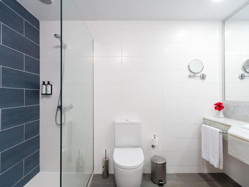 Moderne weiße Toilette in Badezimmer mit Glasdusche, dunklen Fliesen und weißem Waschtisch.