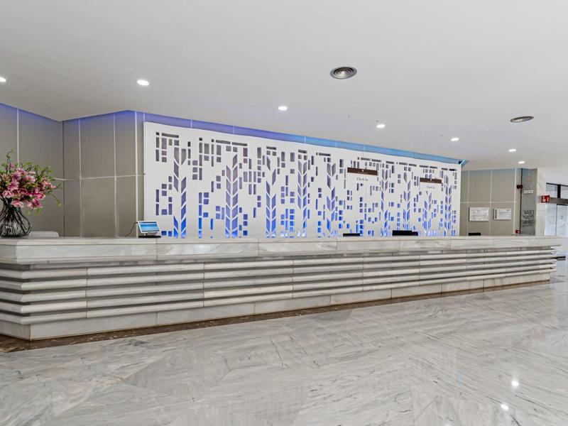 Moderner Empfangsbereich mit langem weißen Tresen, blauen Mosaikfliesen und Blumenarrangement.