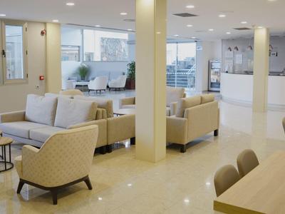 Salotto luminoso dell'hotel con divani beige, poltrone e tavolini in legno.