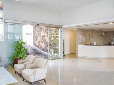 Reception d'hotel luminosa con poltrone bianche e grandi finestre.