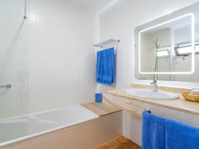 Bagno moderno con vasca, asciugamani blu e specchio illuminato.
