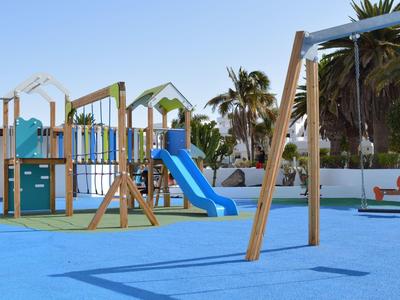 Area giochi esterna colorata con scivolo, altalene e strutture per bambini.