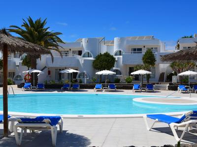 Groot blauw zwembad voor wit hotel met ligstoelen en palmbomen in zonnig resort.