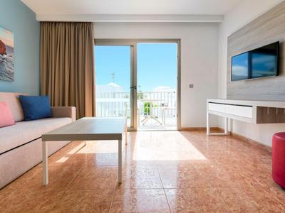 Helles Wohnzimmer mit Sofa, Fenster zur Terrasse und Fernseher an der Wand.