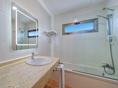 Helles Badezimmer mit beleuchtetem Spiegel, Waschbecken, Badewanne und Fenster für Tageslicht.