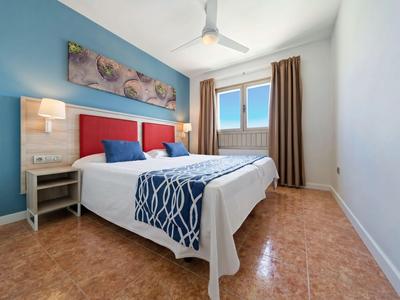 Modernes Hotelzimmer mit zwei Einzelbetten, blauer Akzentwand und Fenster mit braunen Vorhängen.