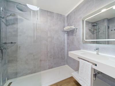 Modernes Badezimmer mit großer Walk-in-Dusche, beleuchtetem Spiegel und weißen Sanitäranlagen.