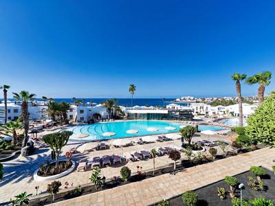 Ein Hotelpool mit Liegestühlen und Palmen vor dem Meer unter klarem blauem Himmel.