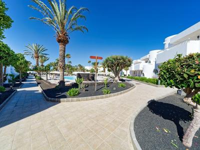 Hotelgarten mit tropischen Pflanzen, Palmen und weißen Gebäuden unter blauem Himmel.