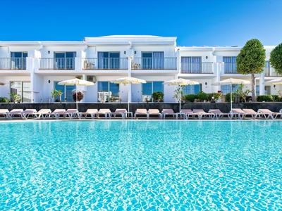 Moderner Hotelkomplex mit großem Pool und Liegestühlen bei klarem Himmel.