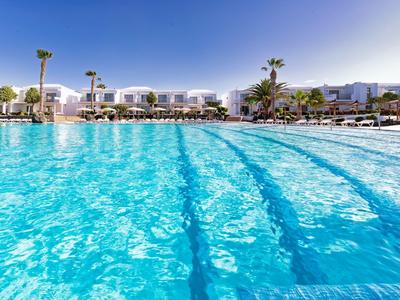 Großer Pool mit klarem Wasser vor modernen Hotelgebäuden unter blauem Himmel.