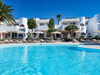 Moderner weißer Hotelkomplex mit Palmen und großem blauem Pool unter klarem Himmel.
