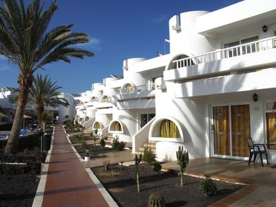 Wit hotelgebouw met ronde balkons en palmbomen langs een pad onder een heldere hemel.