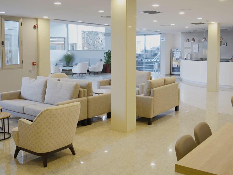 Salotto luminoso dell'hotel con divani beige, poltrone e tavolini in legno.