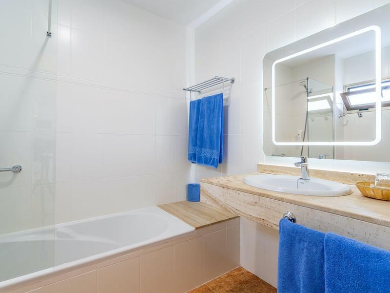 Bagno moderno con vasca, asciugamani blu e specchio illuminato.