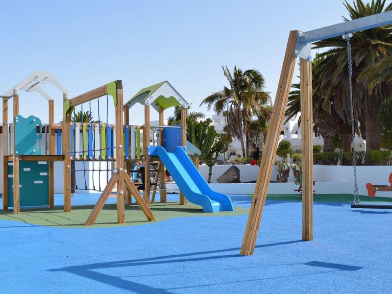 Area giochi esterna colorata con scivolo, altalene e strutture per bambini.