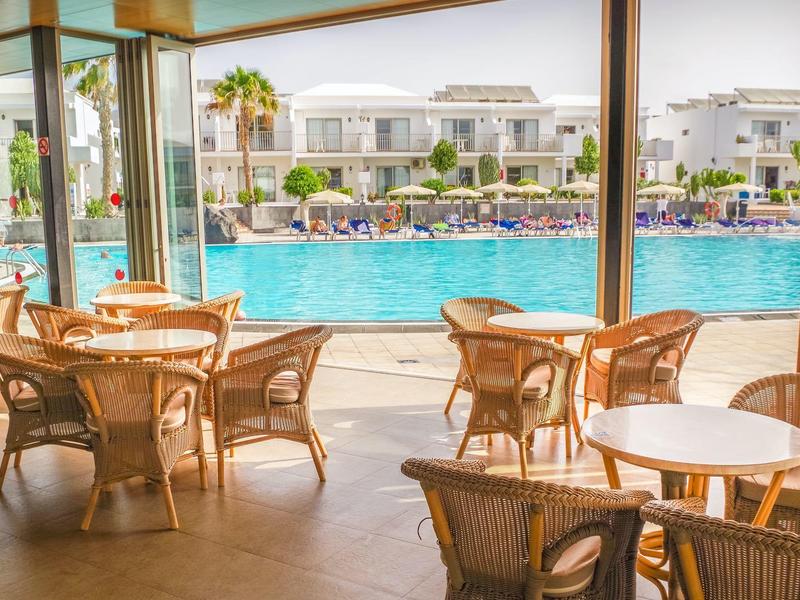 Terrazza del ristorante con tavoli e sedie di fronte a una grande piscina dell'hotel.