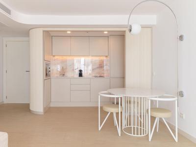 Moderner heller Wohnraum mit eingebauter Küchenzeile und rundem Esstisch mit weißen Stühlen.