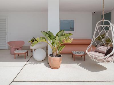 Moderner, heller Wohnbereich mit hängendem Korbsessel, rosa Sofa und Pflanzen in Töpfen.