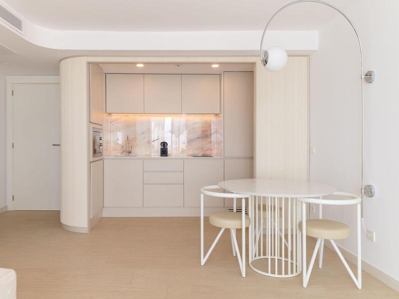 Moderner heller Wohnraum mit eingebauter Küchenzeile und rundem Esstisch mit weißen Stühlen.