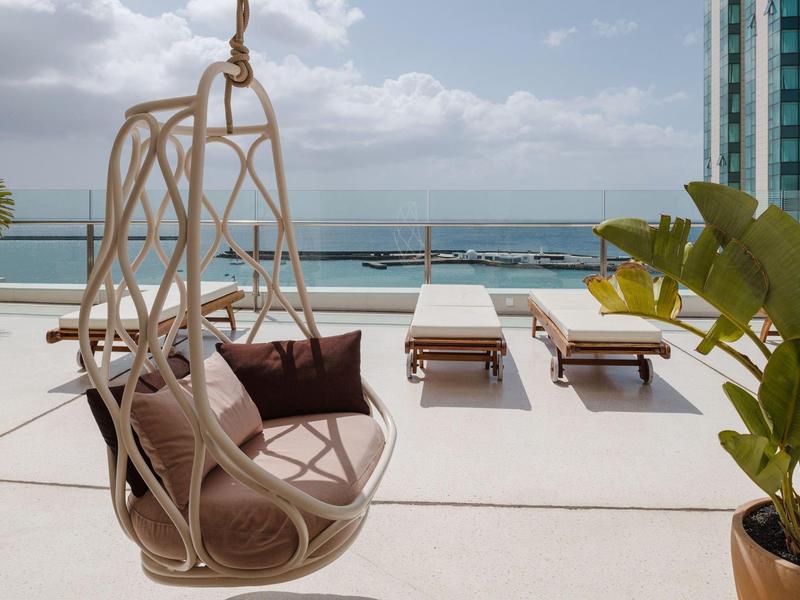 Moderner Balkon mit Hängesessel, Liegestühlen und Meerblick an einem bewölkten Tag