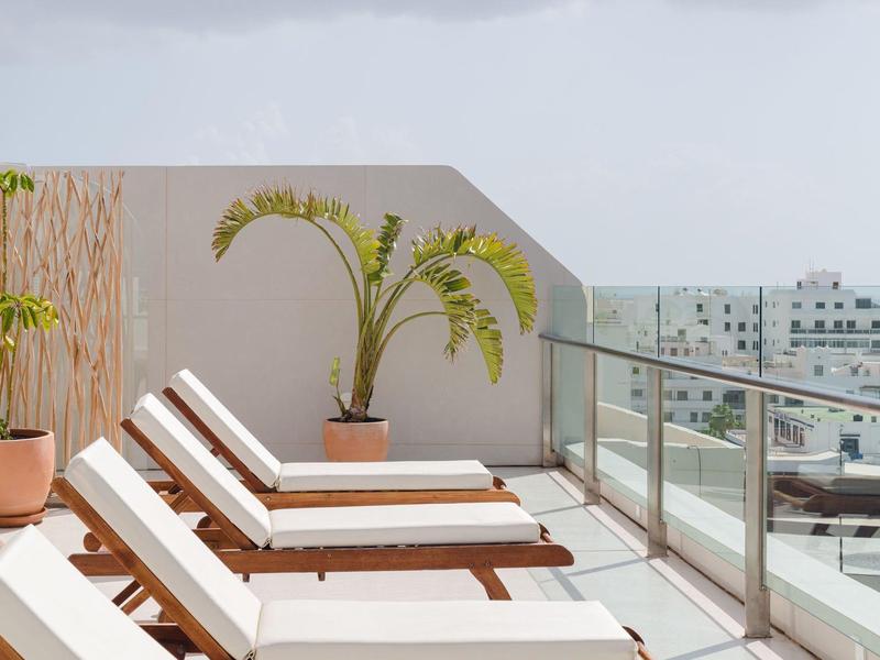 Sonnige Terrasse mit weißen Liegestühlen und Pflanzen auf dem Dach mit Stadtblick.
