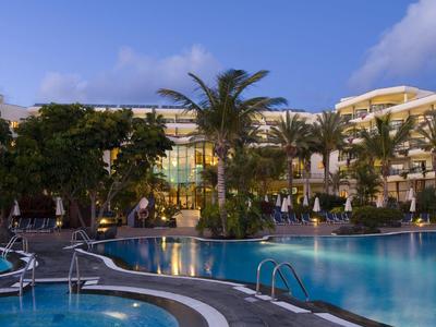 Beleuchteter Hotelpool bei Nacht mit Palmen und ruhiger Atmosphäre.