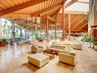 Przestronne lobby hotelowe z drewnianym sufitem, szklanymi ścianami i nowoczesnymi miejscami do siedzenia.