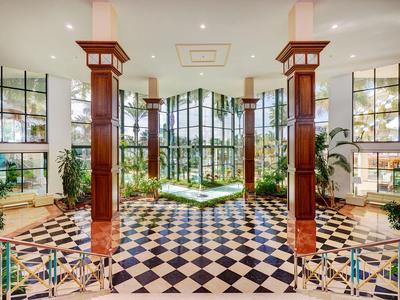 Prostorná hotelová hala s černo-bílou dlažbou a velkými okny