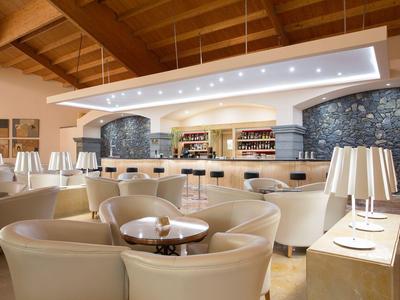 Nowocześnie urządzony bar hotelowy z okrągłymi fotelami i stylowymi lampami pod oświetlonym sufitem.