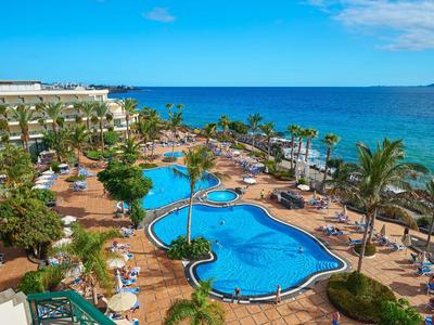 Hotelový resort s několika bazény, palmami a přímým výhledem na moře pod modrou oblohou.