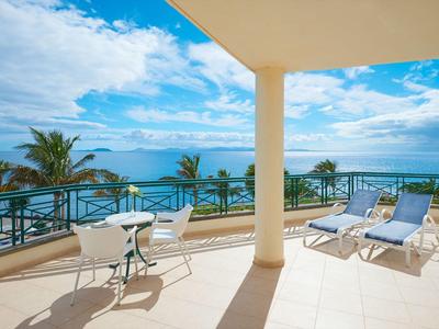 Duży balkon z widokiem na morze, dwie leżaki i stół z dwoma krzesłami.