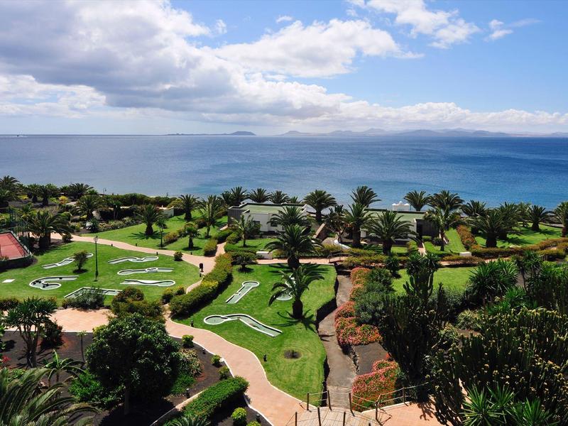 Widok na zadbany ogród z minigolfem przed dużym zbiornikiem wodnym pod pochmurnym niebem.