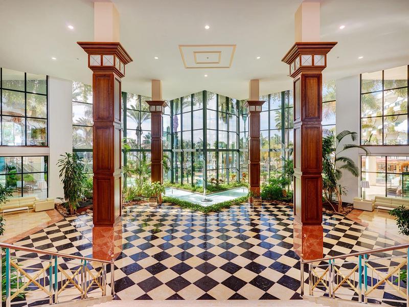 Przestronny hol hotelowy z czarno-białą podłogą i dużymi oknami z widokiem na ogród