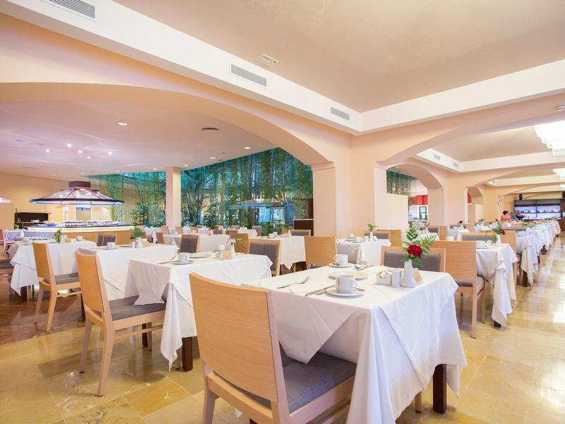 Jasna, elegancka restauracja z nakrytymi stołami i dużymi oknami z widokiem na zieleń.