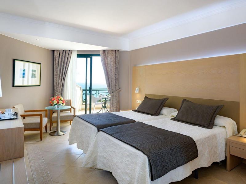 Nowoczesny pokój hotelowy z dwoma pojedynczymi łóżkami, miejscem do siedzenia i balkonem z widokiem na morze.