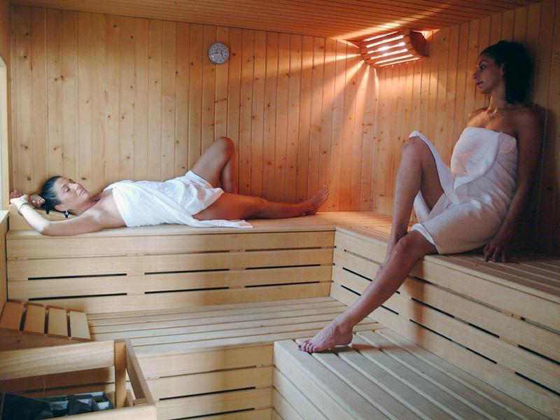Dwie kobiety relaksują się w jasnej, drewnianej saunie z ławkami i małym oknem.