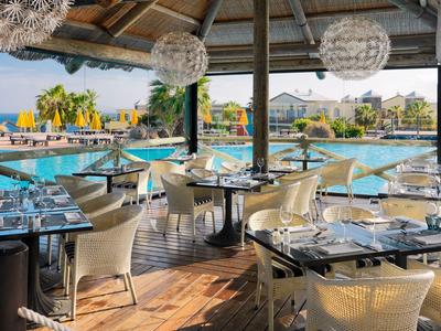 Buitenrestaurant met moderne tafels en stoelen onder een overdekt gebied bij het zwembad.