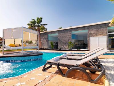 Modern hotel pool area with loungers, cabana, and a sleek building under a clear sky.