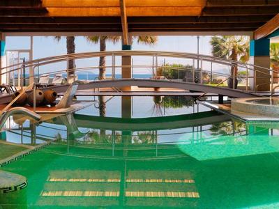 Indoor pool with clear green water and sunlit wooden ceiling beams.