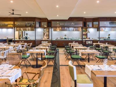 Licht, modern restaurant met hout- en groene accenten en gedekte tafels.