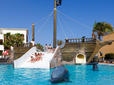 Outdoor pool with a pirate ship play structure and waterslides under clear blue sky.