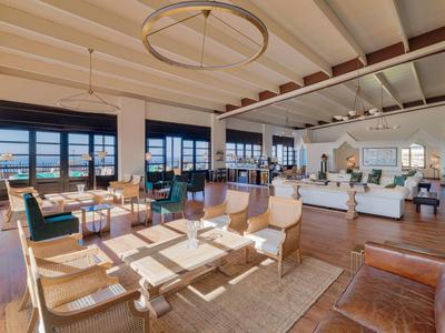 Spacious hotel lounge with modern sofas, wooden chairs, large windows, and sea view.