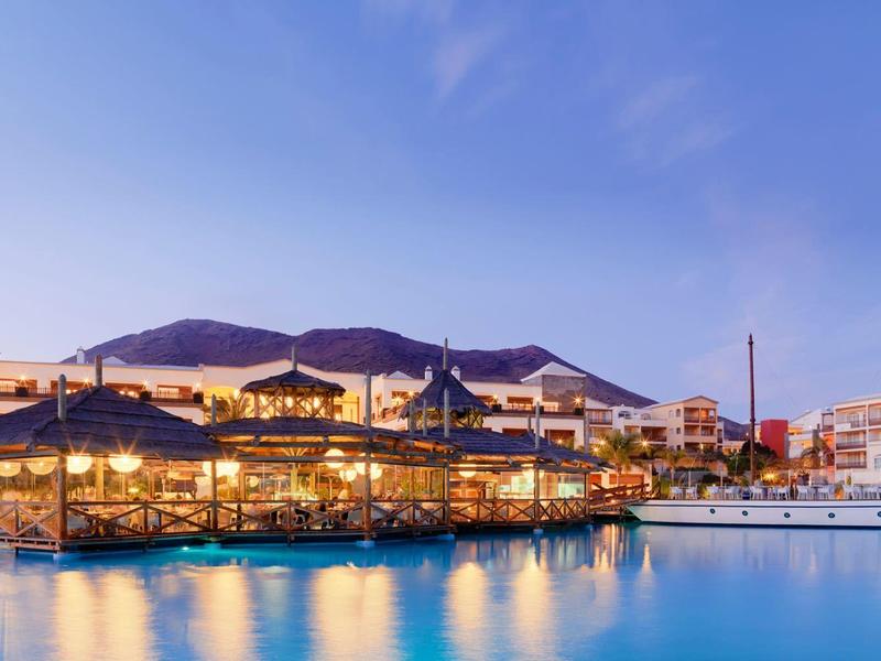 Lakeside resort at dusk with lit buildings and calm water reflecting lights.