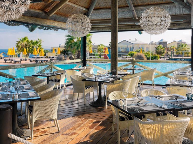 Outdoor dining area with tables, chairs, and pool views at a tropical resort.